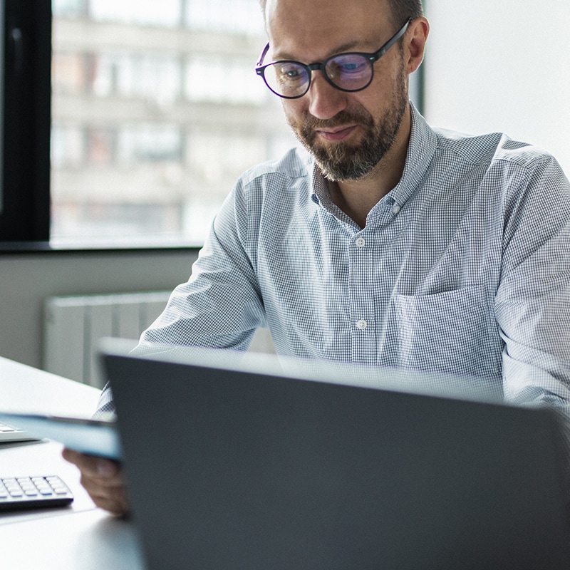 Professional reviewing notes while working on a laptop in a modern office space.