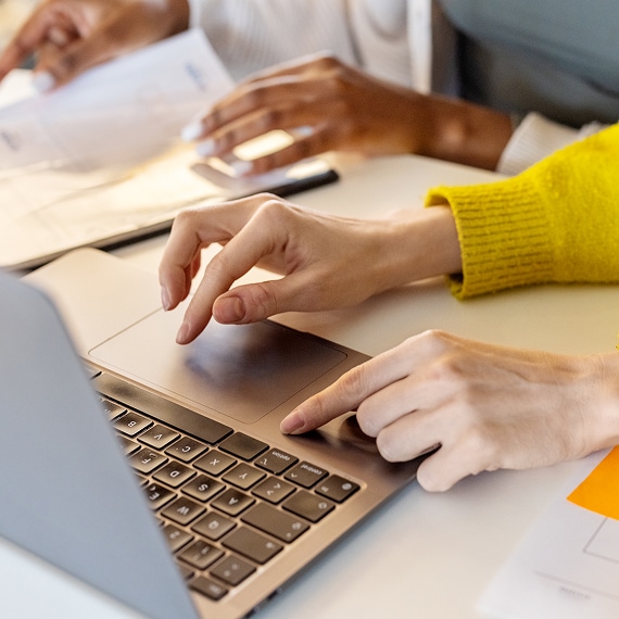 Close-up of hands navigating a laptop trackpad beside printed documents.