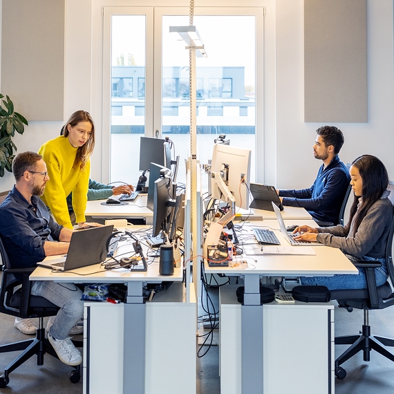 Team collaborating at shared desks with multiple monitors in a modern office.