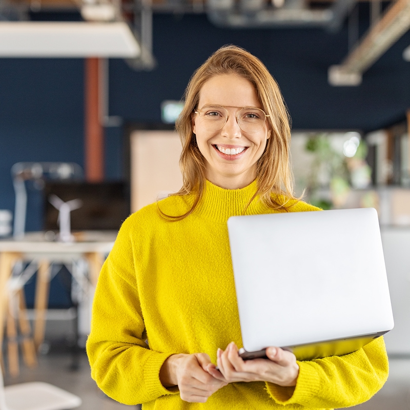 Professional holding a laptop and smiling in a contemporary workspace.