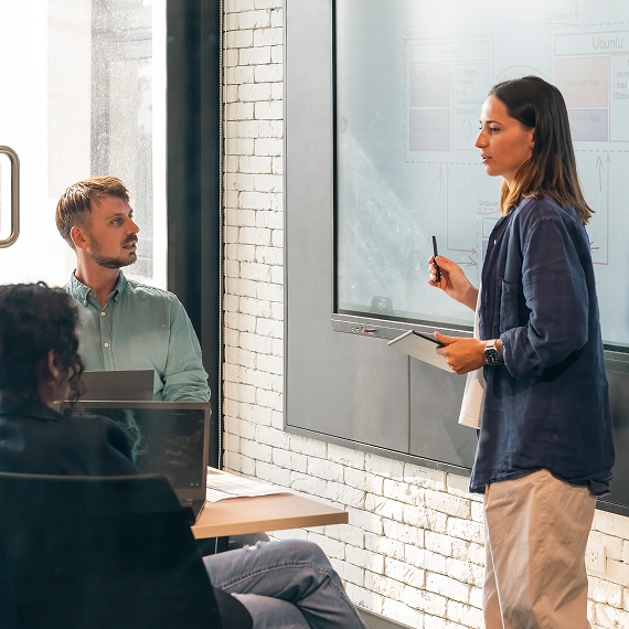 Professional presenting information on a whiteboard during a team meeting in a modern office.