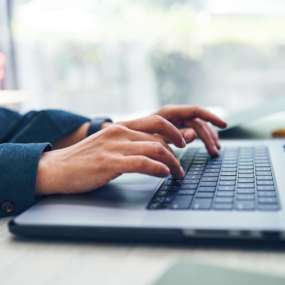 Close-up of hands typing on a laptop keyboard in a bright workspace.