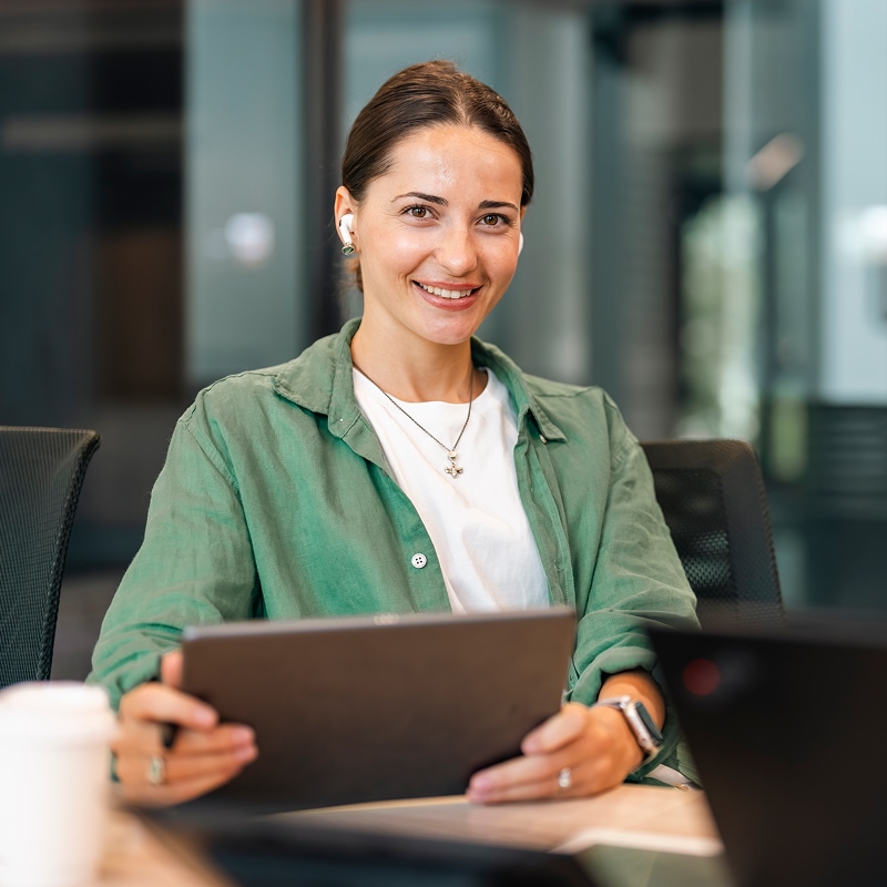 Professional smiling while holding a tablet in a modern office environment.