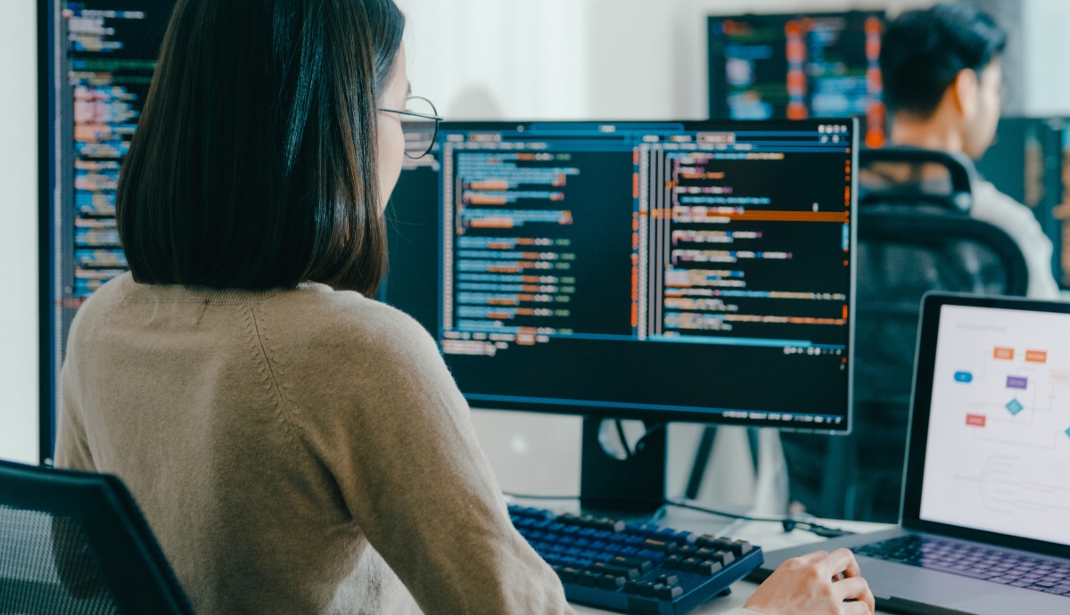 Game developer reviews code across multiple monitors while working at a computer.