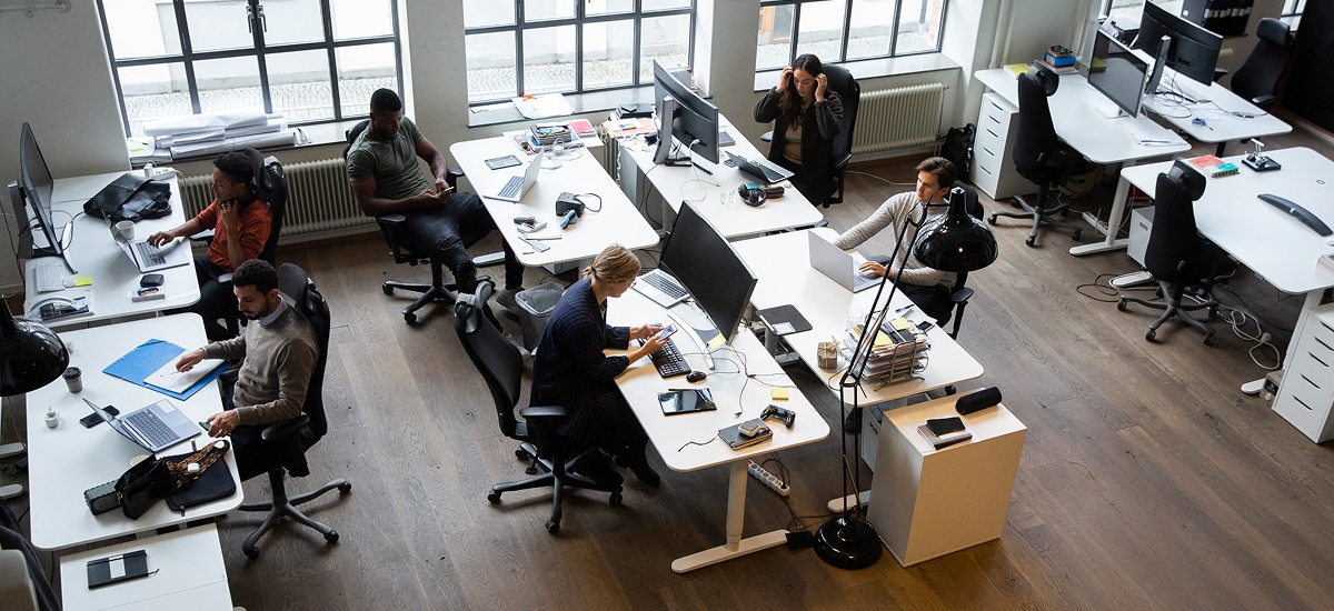 Modern open office with employees working at desks using laptops, phones, and paperwork.