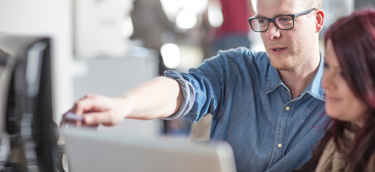 Colleague pointing at computer screen while explaining project details to coworker.