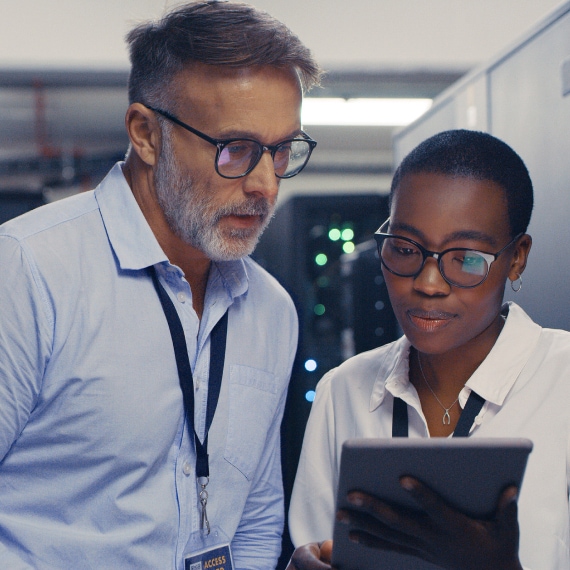 Two IT specialists review system information on a tablet inside a data center aisle.