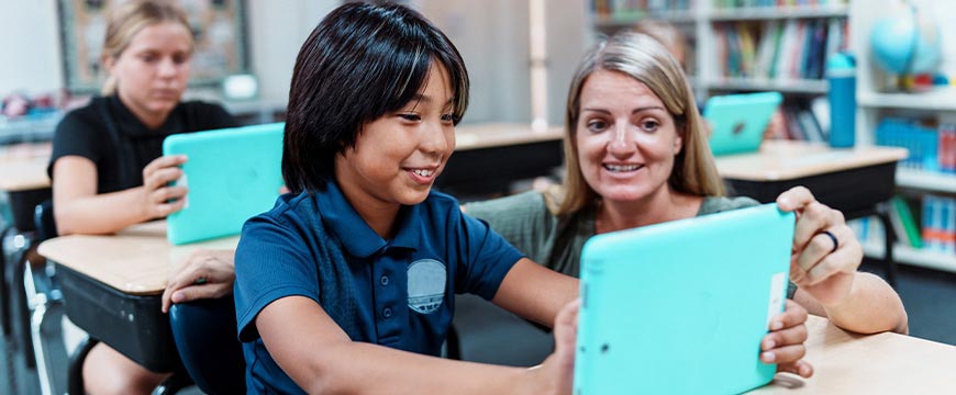 Teacher helps young boy use a tablet in class