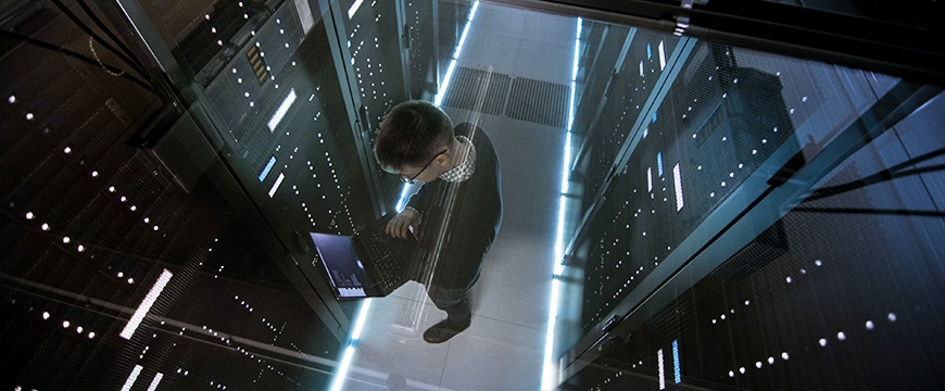 Top View Through the Glass of IT Engineer Working with Laptop in Data Center Full of Active Rack Servers.