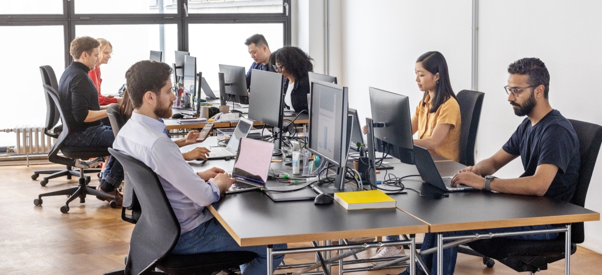 Employees work at computer stations in a collaborative open-plan office environment.