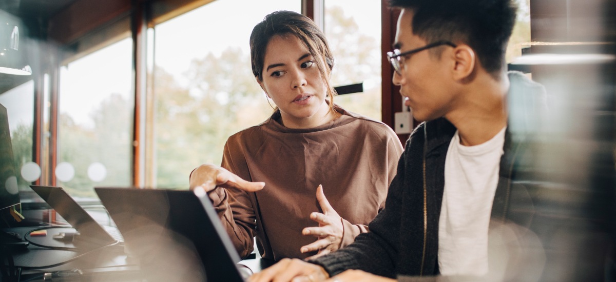 Two colleagues collaborate at a laptop, discussing ideas in a modern office setting.