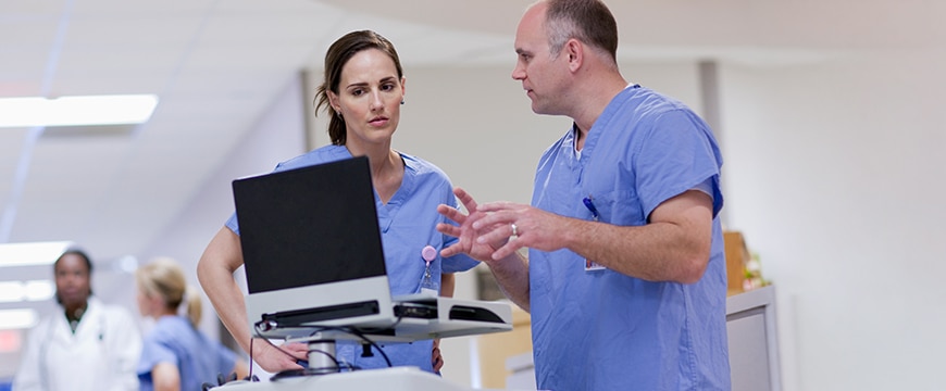 Two nurses working on a portable computer cart in a hospital.