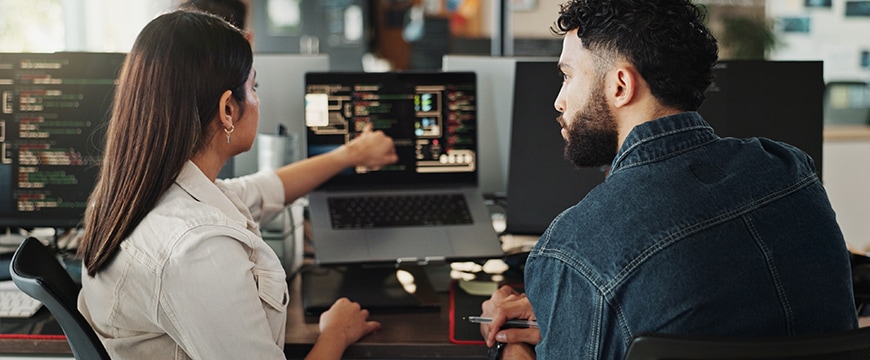 Two programmers collaborating on code in dark office.