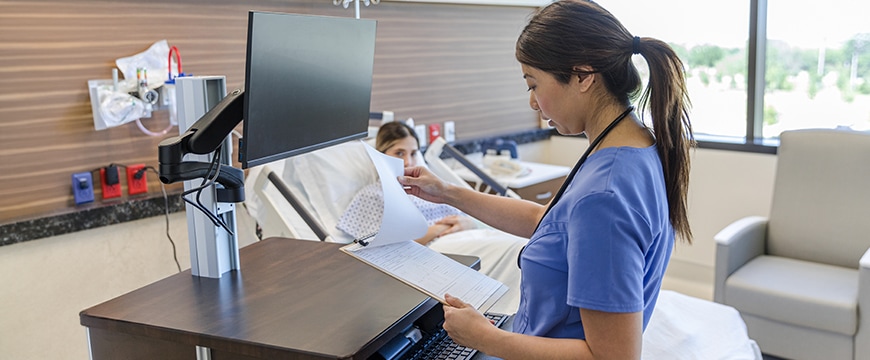 Nurse evaluating patient chart while using computer workstation.