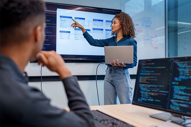 thumbnail image of a woman holding a laptop giving a presentation during an office meeting