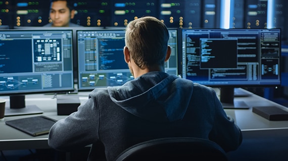Programmer sitting at a computer looking at three monitors.
