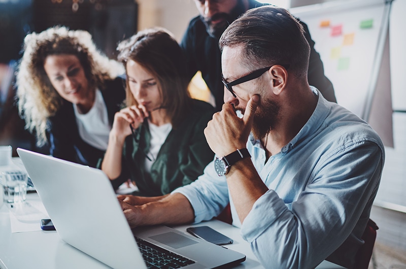 IT professionals collaborating over a laptop in a modern office, representing CDW end‑to‑end device support, lifecycle management, and AI device deployment services