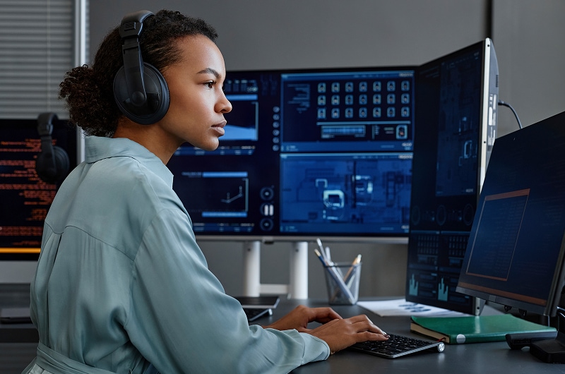 Focused IT professional reviewing data on multiple screens.