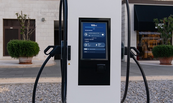 Electric vehicle charging station with integrated digital screen in a public area.