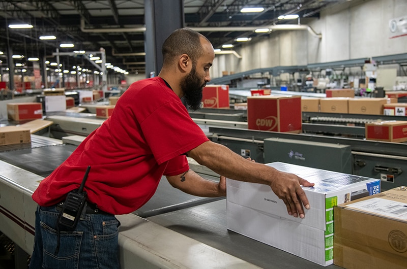 Person in CDW warehouse unloading a box from a conveyor belt.