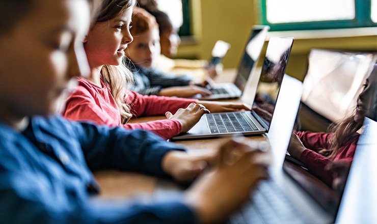 Children sit at desks and work on laptops