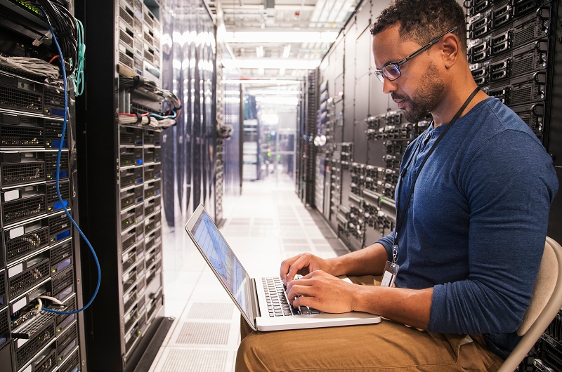 IT professional working on laptop in server room.