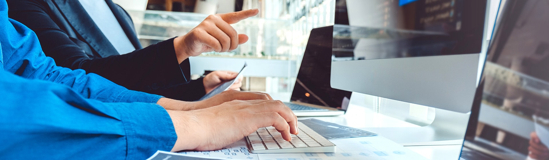 Close up image of a person typing on a keyboard and another person pointing at computer screen.