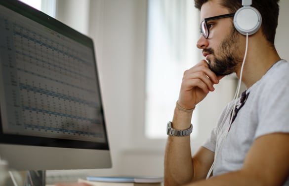 Close up image of a man with headphones looking at computer screen.