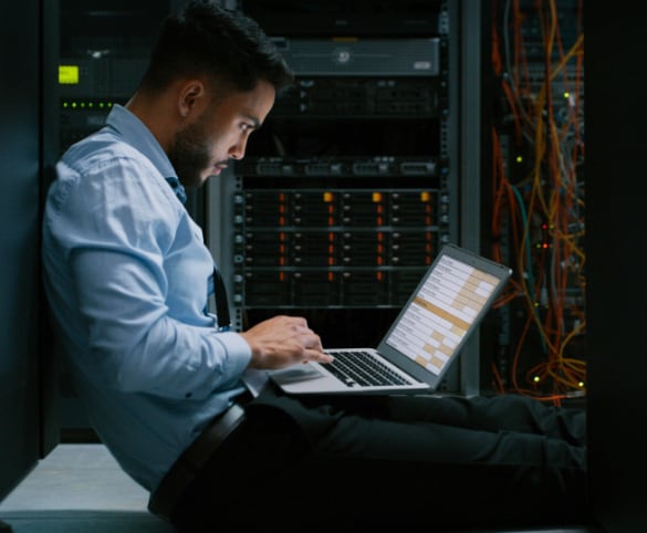 IT manager in server room using a laptop.