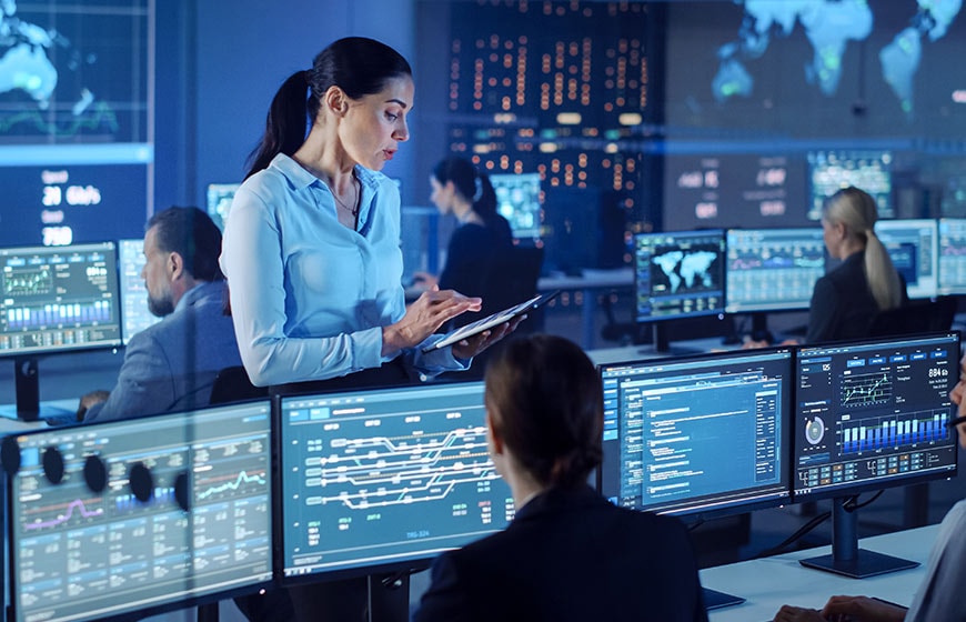 Close up image of a woman at her desk speaking to a smart speaker.