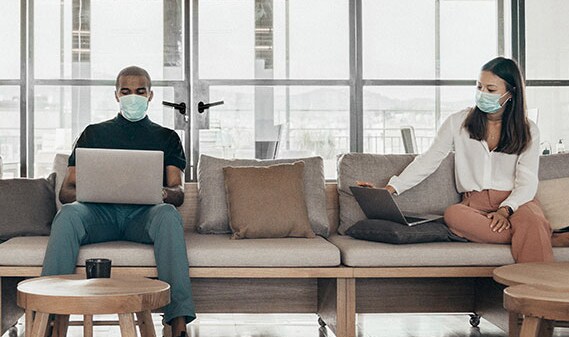 Two people working on laptops wearing masks
