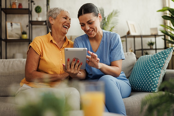 Senior woman reviewing details on a tablet from her female caregiver at home