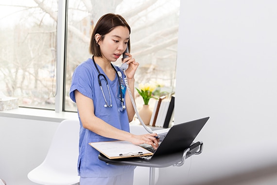 Female nurse on the phone with a patient while reviewing details on a laptop