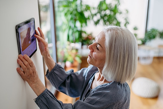 senior woman using a wall mounted tablet to control her smart thermostat