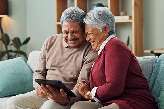 Senior couple sitting on the couch using a handheld tablet