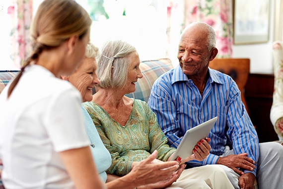 a group of seniors talking while holding a tablet with a nurse