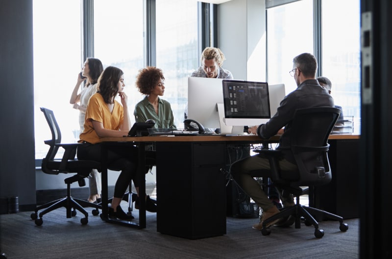 Small business team working together using desktop computers in a meeting room.