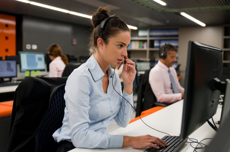 A 911 operator is speaking on the phone while looking at a computer screen.