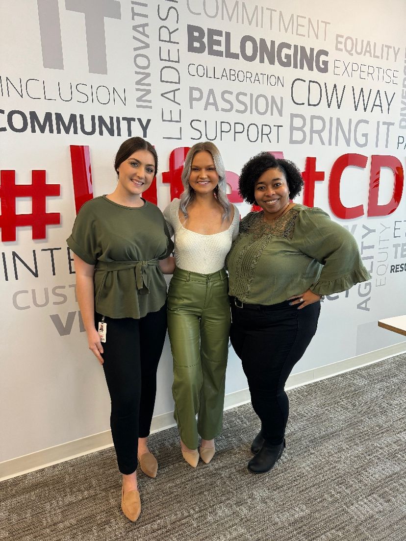 Three coworkers pose for a photo in front of a branded wall.