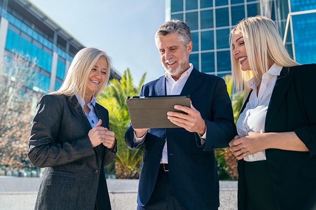 Group of government employees looking at a tablet outside of a building.