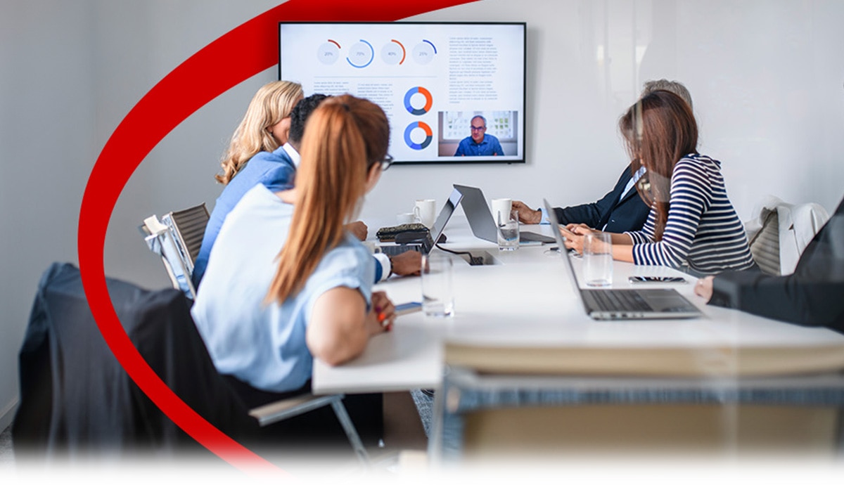 A team of business professionals is having a video conference on a large screen on the wall.