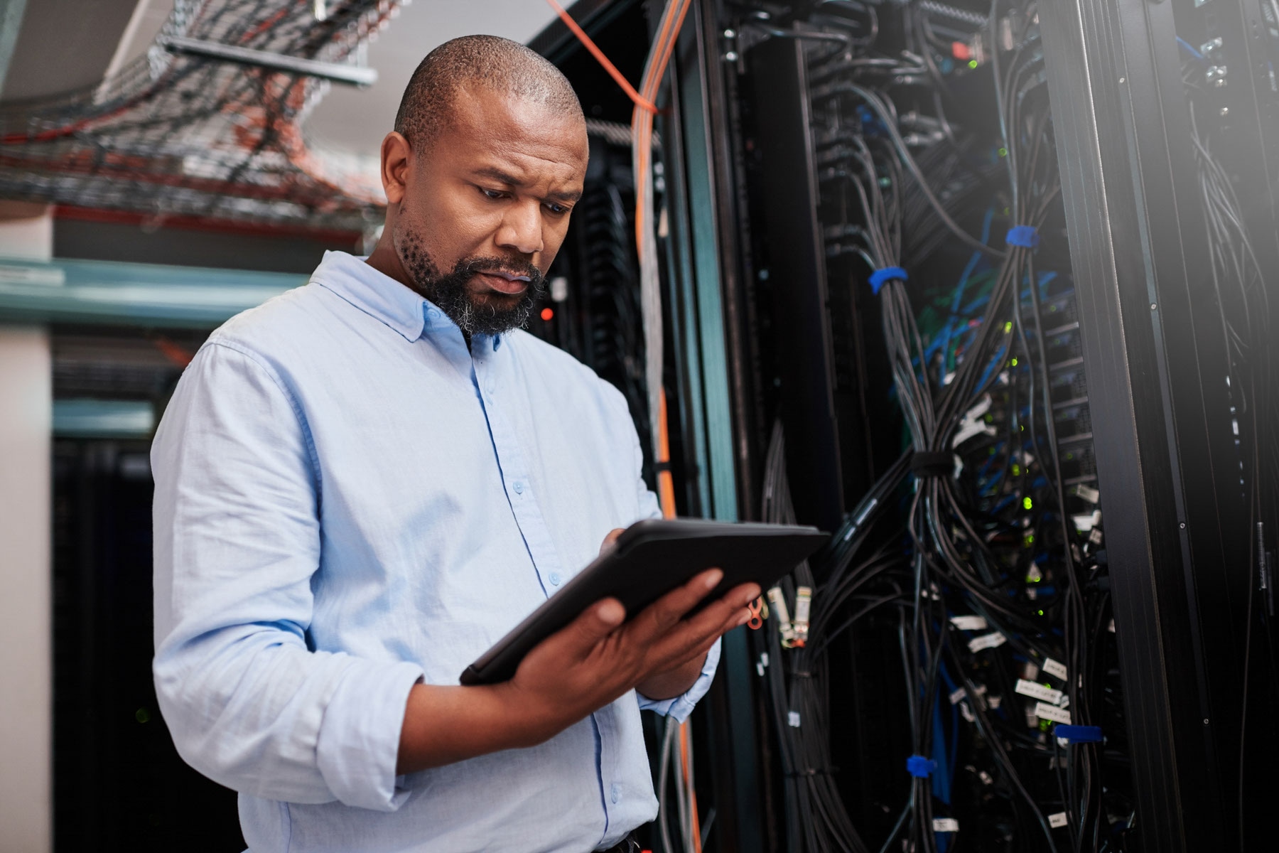 Person standing in data centre looking at a digital tablet, with a serious expression.