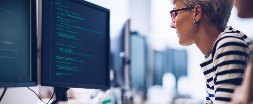 Person working at computer monitors displaying software code in office workspace