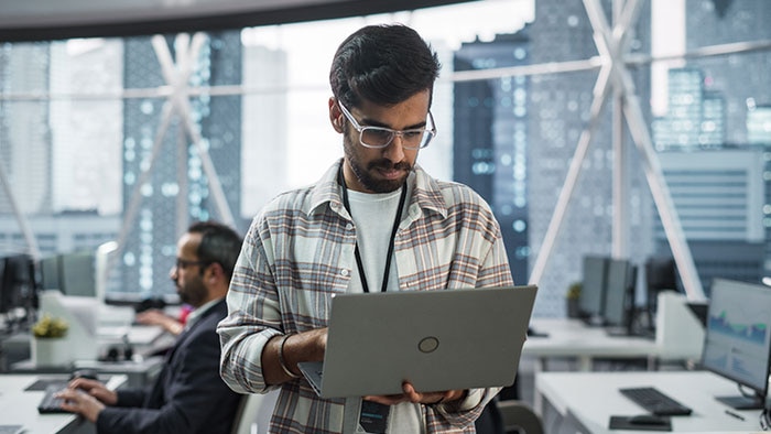 Software developer working on a laptop in a modern office, representing the software development lifecycle from planning and design through development, testing, deployment and maintenance.