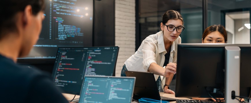 IT professionals reviewing code and monitoring computer systems in an office environment to strengthen network security and protect against cyber threats.