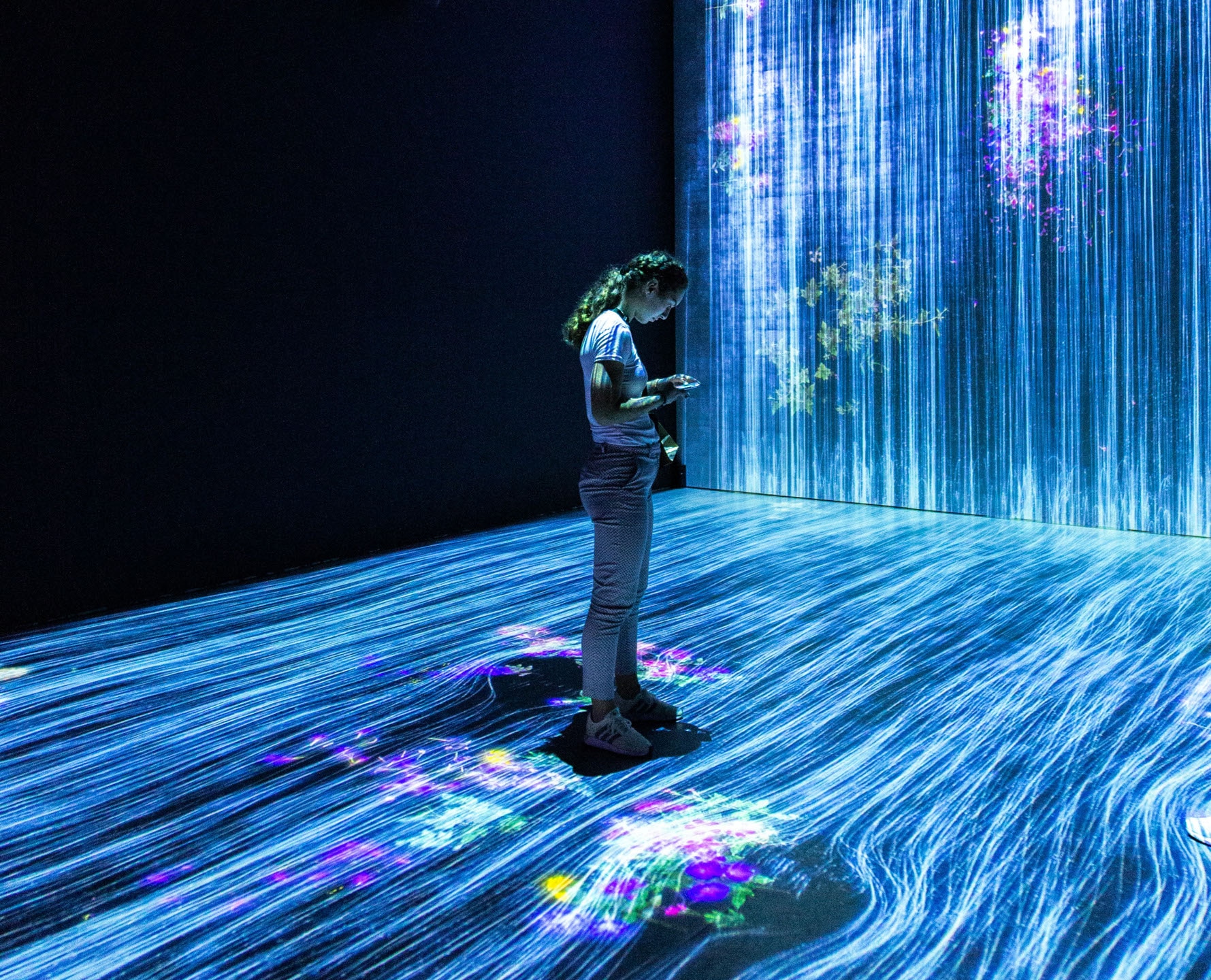 Girl standing in an i interactive art gallery with fibre like light projections scattered across the room.