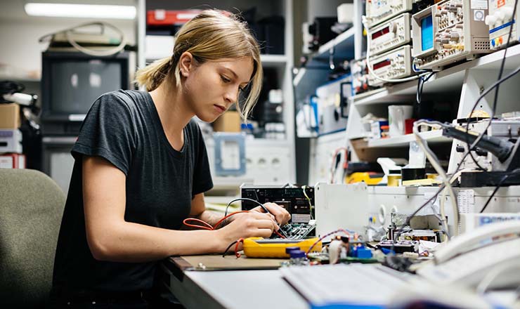 Woman in computer server room modifies technology at a desk