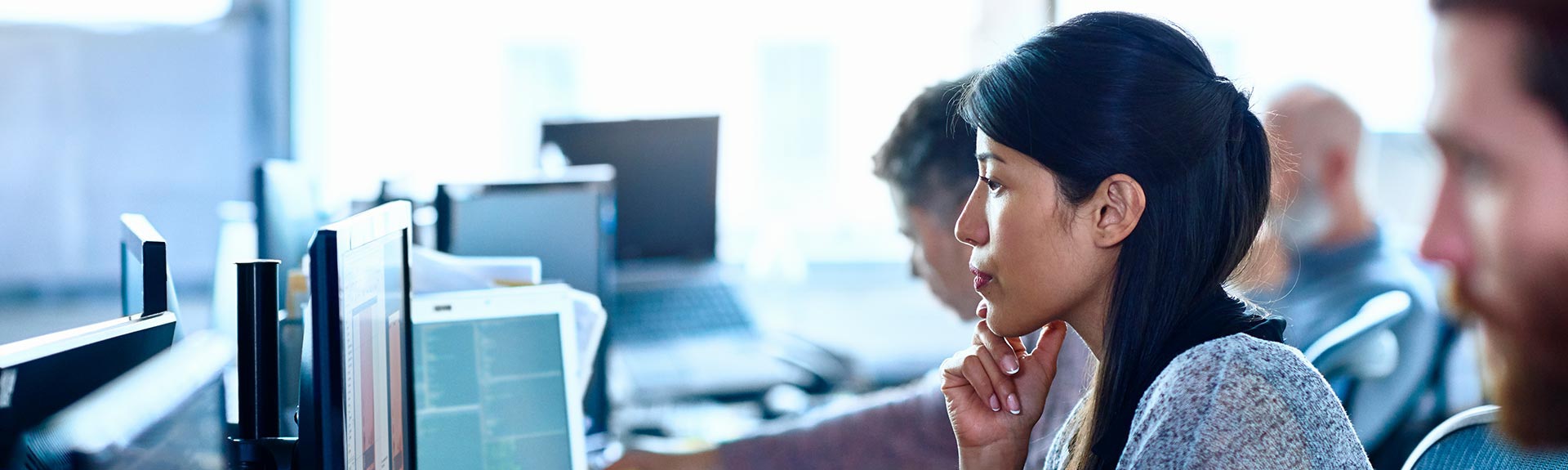 Woman sitting in an office while looking at a computer with a serious expression.