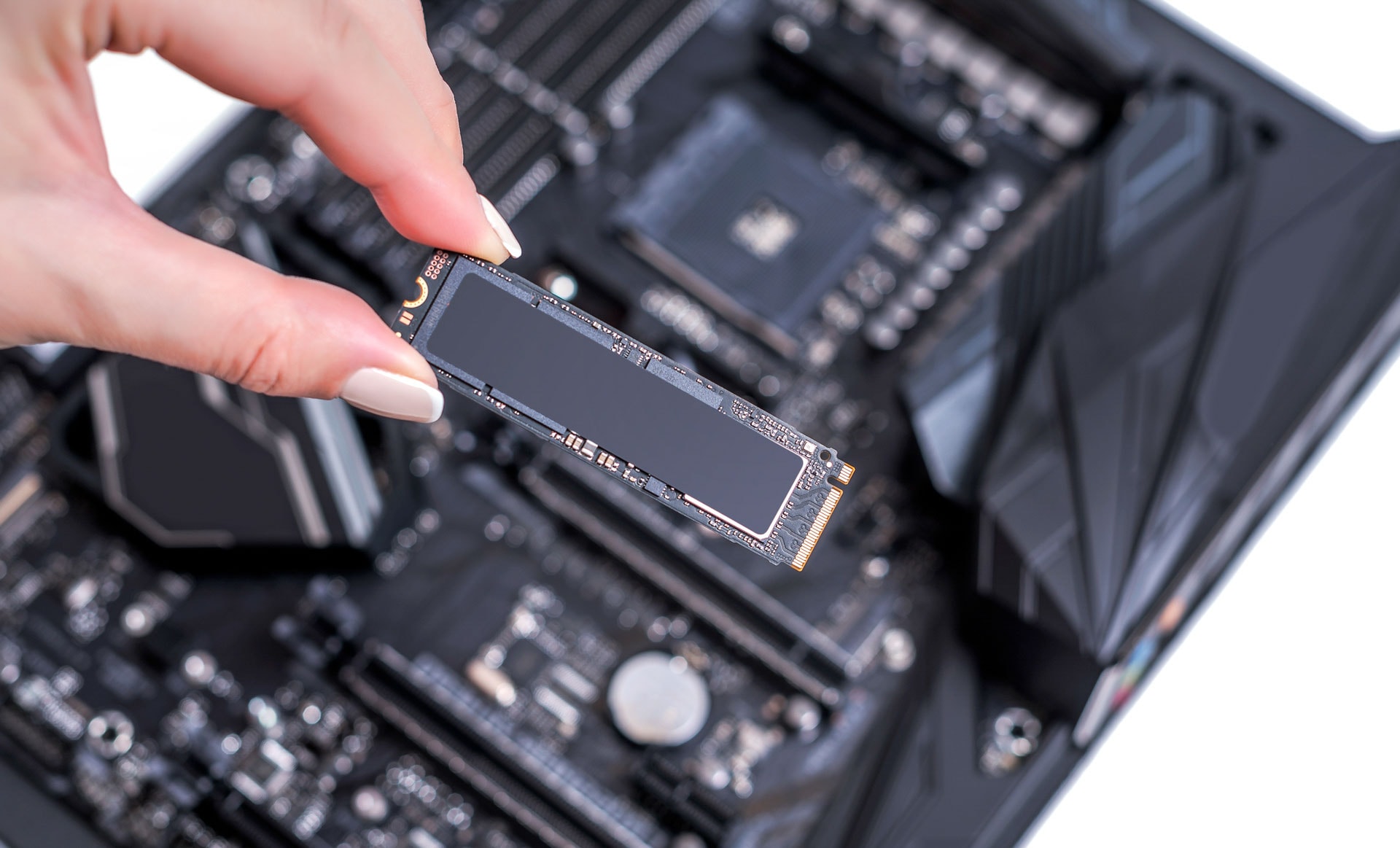 Lady holding an M.2 SSD in front of the camera with a computer motherboard in the background.